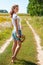 Beautiful blonde girl walking barefoot on summer field with a bouquet of wild flowers