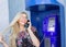 A beautiful blonde in glasses is holding a telephone receiver in a payphone. Beautifully smiling and talking on the phone.