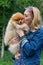 A beautiful blonde holds and kisses a small Pomeranian dog on a walk in the Park
