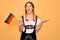 Beautiful blonde patriotic woman with blue eyes wearing octoberfest dress holding german flag very happy and excited, winner