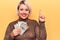 Beautiful blonde plus size woman holding bunch of dollars banknotes over yellow background smiling with an idea or question