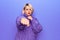 Beautiful blonde plus size woman wearing casual turtleneck sweater over purple background Punching fist to fight, aggressive and