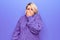 Beautiful blonde plus size woman wearing casual turtleneck sweater over purple background smelling something stinky and