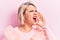 Beautiful blonde plus size woman wearing pincess tiara with diamonds over pink background shouting and screaming loud to side with