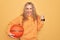 Beautiful blonde sportswoman doing sport holding basketball ball over yellow background screaming proud, celebrating victory and