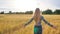 A beautiful blonde teen girl runs across a wheat field and turns around and smiles.