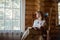 A beautiful blonde woman in beige home clothes sits in a cozy rocking chair and reads a book. Cozy village life. Room