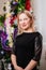 beautiful blonde woman in black dress by Christmas tree. single unmarried woman.