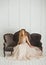 Beautiful blonde woman with greek hairstyle in beige powdery atlas wedding dress posing in studio room