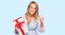 Beautiful blonde woman holding gift annoyed and frustrated shouting with anger, yelling crazy with anger and hand raised