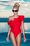 Beautiful blonde woman model with amazing body standing in the pool in an elegant red swimsuit