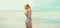 Beautiful blonde woman model looking away wearing sunglasses, striped dress on sea coast background