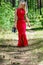 Beautiful blonde woman in red dress and black shoes in hand walks through the forest