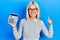 Beautiful blonde woman showing calculator device smiling happy and positive, thumb up doing excellent and approval sign