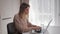 Beautiful blonde woman sitting at home kitchen workplace typing on laptop.