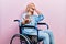 Beautiful blonde woman sitting on wheelchair covering eyes with hands and doing stop gesture with sad and fear expression