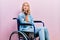 Beautiful blonde woman sitting on wheelchair looking at the camera blowing a kiss with hand on air being lovely and sexy