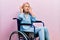 Beautiful blonde woman sitting on wheelchair trying to hear both hands on ear gesture, curious for gossip