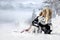 Beautiful blonde woman, standing on snow and holding Husky dogs view of mountains and snow.