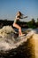 Beautiful blonde woman wakesurfer riding on splashing wave on a warm day