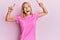 Beautiful blonde woman wearing casual pink tshirt smiling amazed and surprised and pointing up with fingers and raised arms