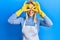 Beautiful blonde woman wearing cleaner apron and gloves doing ok gesture like binoculars sticking tongue out, eyes looking through