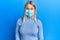 Beautiful blonde woman wearing covid-19 medical mask looking positive and happy standing and smiling with a confident smile