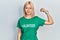 Beautiful blonde woman wearing volunteer t shirt strong person showing arm muscle, confident and proud of power