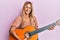 Beautiful blonde young woman playing classical guitar smiling with a happy and cool smile on face