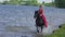 A beautiful blonde young woman in a red dress riding a horse at a lake.