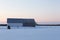 Beautiful blue hour winter view of patrimonial grey barn with steep metal roof in snowy field