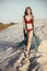 beautiful boho girl in red swimsuit walking on sandy beach at sunset light. attractive young woman in bohemian look with win