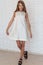 Beautiful bold fashionable girl in white dress in trendy black shoes posing near a white brick wall in the Studio