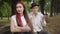 Beautiful bored sarcastic woman sitting on bench with blurred man resenting at the background. Portrait of young