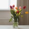Beautiful bouquet of tulips in glass vase on white table in a cozy room interior. Blooming flowers decoration in living