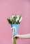 Beautiful bouquet of tulips and roses in blue packing in a female hand on pink background