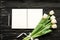 Beautiful bouquet of white tulips and open notebook, silver pen on the black wooden background