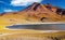 Beautiful brackish water lake in andes high plains, rugged red orange mountain, yellow dry grass tufts - Laguna Miniques, Atacama