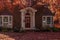 Beautiful brick house with bay windows and columns and wreath of red front door in shadow of maple trees in autumn - yard covered