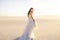 A beautiful bride in a beautiful long dress walks on the sand in the desert