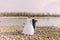 Beautiful bride closing eyes of elegant groom near river with stones. Wedding couple in love