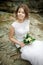 Beautiful bride with disheveled hair on stones among rocks, wedding bouquet in hands. Candid portrait.