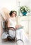 A beautiful bride in elegant white dress sitting in a armchair and dreams of a wedding day. Romantic bridal morning