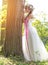 Beautiful bride , flower tiara on her head , relying on the tree