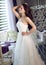 Beautiful bride in a magnificent white wedding dress of tulle with a corset sitting on the sofa with bouquet lily and orchid