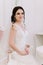 Beautiful bride perfect style. Wedding hairstyle make-up dress and bride`s bouquet. Young attractive bride on chair in white room