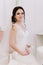 Beautiful bride perfect style. Wedding hairstyle make-up dress and bride`s bouquet. Young attractive bride on chair in white room