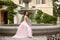 Beautiful bride in pink prom dress by round fountain. Outdoor romantic portrait  of Attractive brunette woman with makeup and