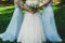 Beautiful bride in puffy dress and veil is holding pastel elegant bouquet in her hands. her bridesmaids in lace light blue dresses