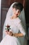 Beautiful bride with stylish hairlock posing when holding cute floral boutonniere in dressing room